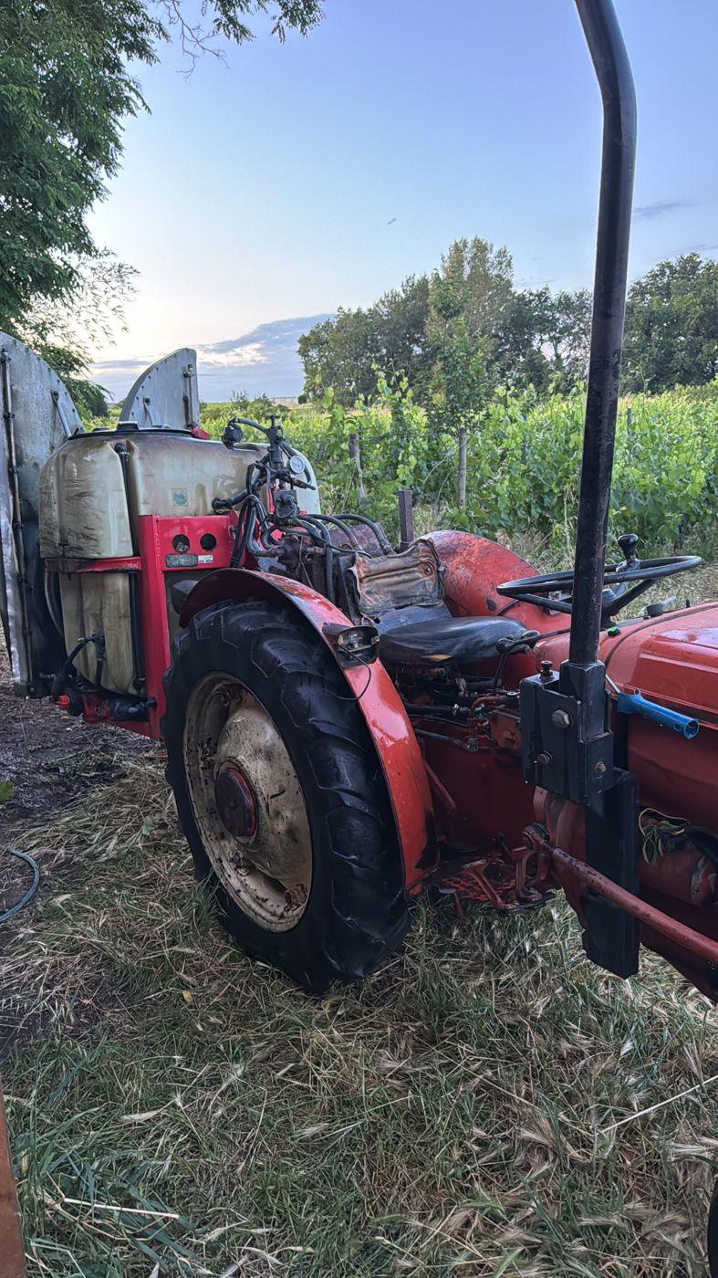 Vieux tracteur Renault rouge équipé d'un pulvérisateur, au bord des vignes en feuilles